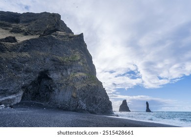 The iconic Reynisdrangar sea stacks rise dramatically from the black sand beach of Reynisfjara in Vik, Iceland. These basalt columns contrast sharply with the turbulent ocean and the rugged cliffs. - Powered by Shutterstock