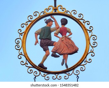 Iconic Sign Of An Austrian Traditional Dancing Couple In Salzburg, Shows Golden Frame, Lederhosen And Dirndl