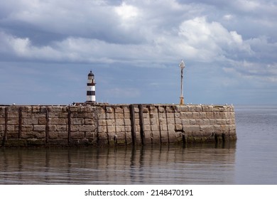 Iconic striped Seaham lighthouse on sea wall with cloud reflections
