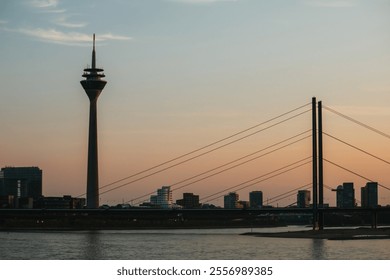 Iconic telecommunications tower and suspension bridge at sunset, with a calm river and modern city skyline in the background. - Powered by Shutterstock