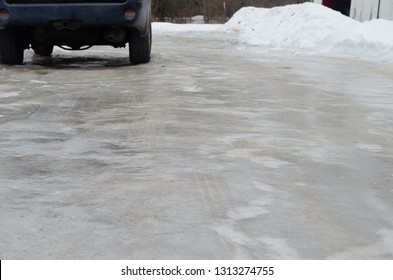 Icy Ice Covered Driveway With Snow After Storm In Winter With Dark Blue SUV Car Parked.