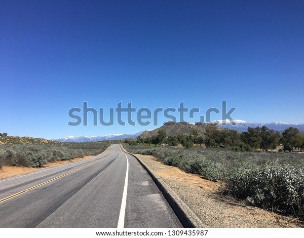 The icy Mountain\
View.  The street has yellow dividers in the middle. There are\
bunches and trees on the side. The sky is clear and blue. The\
street are covered with\
asphalt.