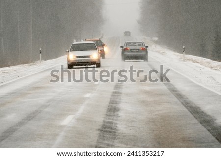 Icy road danger: cars meeting head-on in snowy conditions. Unsafe winter road: oncoming traffic in snowy weather. Two cars on collision course in snowstorm. 