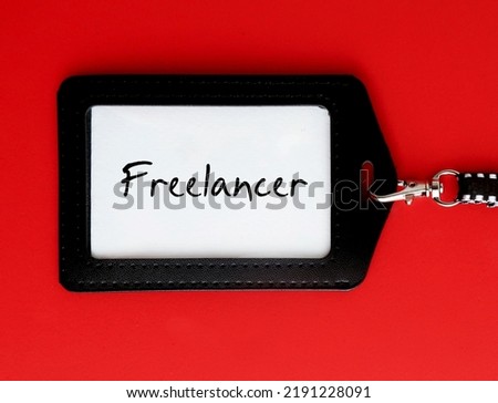 ID card holder on red background with job title text FREELANCER - freelance worker who is self-employed, not committed to particular employer