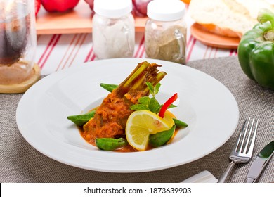 Idam bamia is basically a middle eastern meat lamb and okra stew. It is served with okra, bell pepper and mint leaves over a round white plate, dinner mat and red stripe napkin.