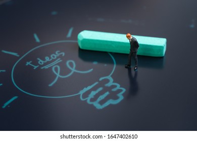 Idea, brainstrom or business solution concept, miniature people businessman in suit standing and thinking on chalkboard with chalk writing light bulb and the word ideas.