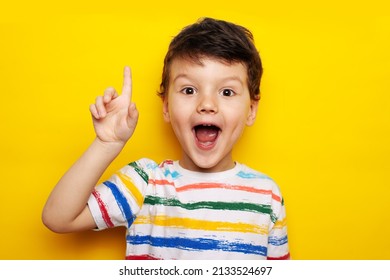 idea. child, boy emotionally points up. A gesture of an idea. Portrait of a child in a bright striped T-shirt on a yellow background, studio - Powered by Shutterstock