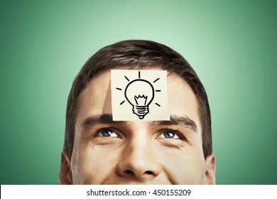 Idea concept with lightbulb sketch drawn on sticker glued to happy guy's forehead on green background
