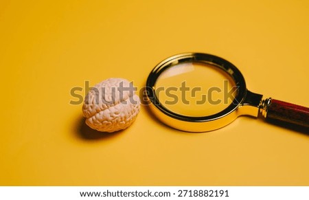 Idea concept. Miniature brain model and magnifying glass on yellow background symbolizing intelligence and research.