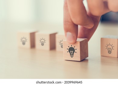  Idea and creativity concept. Male hand holds wooden cube with light bulbs icon on light background. Teamwork brainstorming ideas, evaluation and selection for business development. Banner, copy space