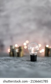 idea light bulb with stacks of different golden and silver coins representing a big amount of money shot on grey concrete background with fairy light, success and abundance concept