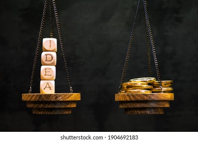 The idea is on the scale in a counterbalance with yellow shiny coins on another bowl on a dark background. Background. The concept of the value of an idea, its sale, making money, investing, and so on