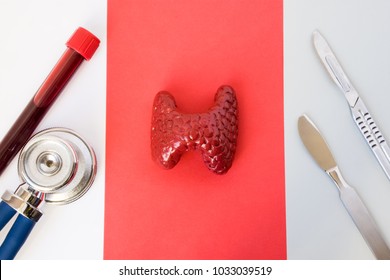 Idea of photo diagnosis, thyroid gland surgery or operation. Thyroid gland anatomical figure model lies near stethoscope, laboratory test tubes with blood and two scalpels on white red gray background