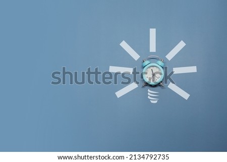 Idea symbol in the form of a painted light bulb with an alarm clock inside on a blue background. Time to think