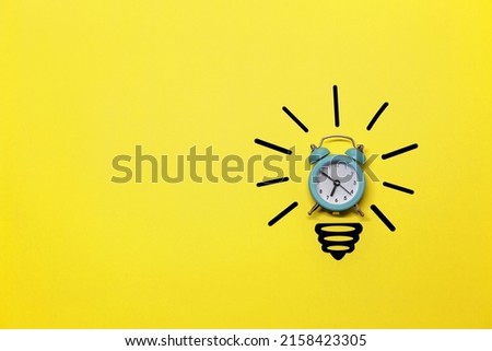 Idea symbol in the form of a painted light bulb with an alarm clock inside on a yellow background. Time to think.