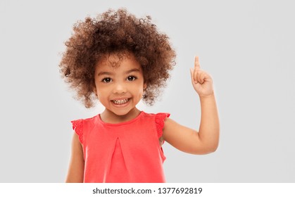 idea, warning and childhood concept - happy little african american girl pointing finger up over grey background