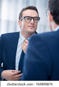 Ideal Look. Pretty Cute Happy Man Touching His Tie While Staring At The Mirror And Wearing Glasses 