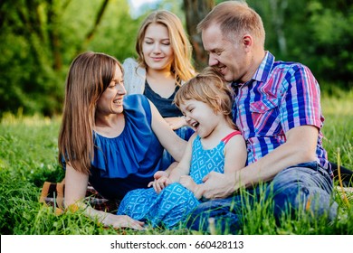 Ideal Picture Of Family Happiness - Happy Family With Two Daughter Having Fun And Lying On The Grass On A Summer Day In Sunset. Parenthood, Love, Vacation And Happy Family Concept.