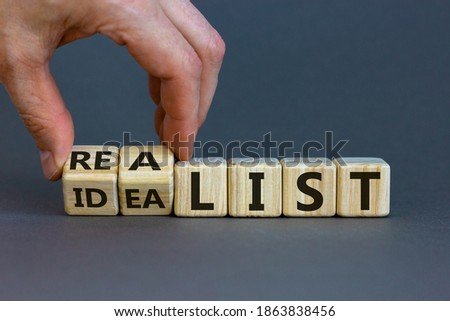 Idealist or realist. Male hand flips wooden cubes and changes the word 'idealist' to 'realist' or vice versa. Beautiful grey background, copy space. Idealist or realist concept.