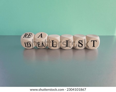 Idealist or realist. Turned wooden cubes and changes the red word 'idealist' to 'realist' or vice versa. Beautiful blue background, grey table. Copy space. Idealist or realist concept.