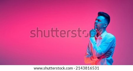 Ideas. Flyer with portrait of young handsome man in white shirt thinking, praying isolated over magenta color studio background in blue neon light. Concept of youth, fashion, emotions, facial