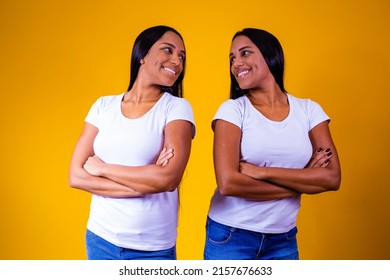 Identical Twin Sisters On Yellow Background With Arms Crossed