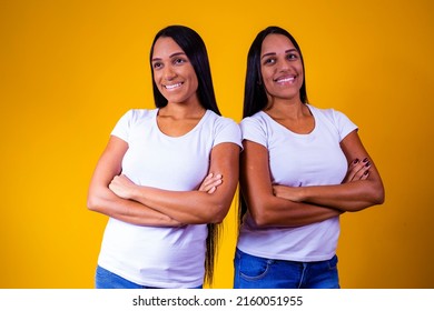 Identical Twin Sisters On Yellow Background With Arms Crossed