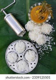 Idiyappam, String hoppers, Noolappam- Traditional Kerala steamed healthy breakfast served with mutton stew on a banana leaf. Stainless steel press maker and idli mould nearby.