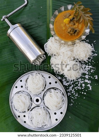 Idiyappam, String hoppers, Noolappam- Traditional Kerala steamed healthy breakfast served with mutton stew on a banana leaf. Stainless steel press maker and idli mould nearby.