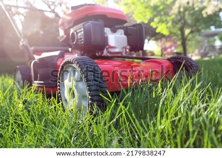 Idle lawnmower letting grass grow, concept of preservation and creating habitat for pollinators such as insects and bees, shallow focus on grass blades near wheel