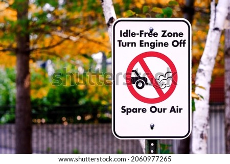 Idle-Free Zone, Turn Engine Off Sign at street parking against blurred autumn colours.