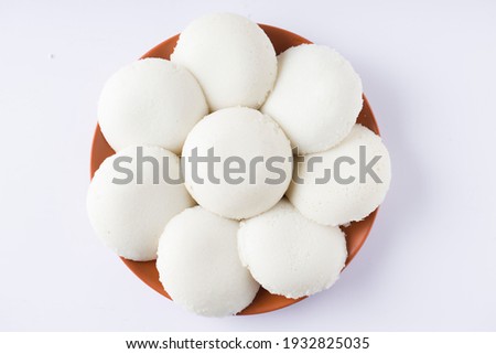 Idly or Idli, south indian main breakfast item which is beautifully arranged in an earthen ware with  white background.