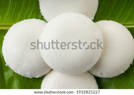 Idly or Idli, south indian main breakfast item which is beautifully arranged in a fresh green banana leaf on white background.
