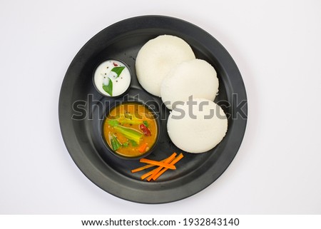 Idly or Idli, south indian main breakfast item which is beautifully arranged in a black plate on white background.