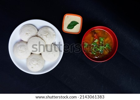 Idly In White Plate, Sambar In Red Bowl with Coconut Chutney In Bowl, Isolated On Black Background