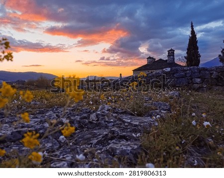 Idyllic countryside sunset view with dramatic sunset sky and clouds,a rural church silhuette, and yellow wildflowers blooming in the field