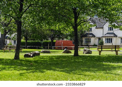Idyllic English country house, lush green lawn, dappled sunlight through trees, wooden bench, vintage red car, old house walls in the background. - Shutterstock ID 2333866829