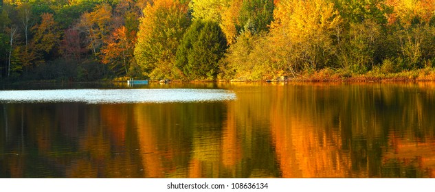 Idyllic Fall Foliage Scene With Reflections On Lake With A Wisp Of Wind Ripples.