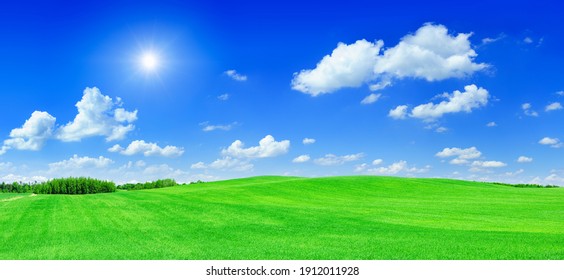 Idyllic landscape, sun shining over green rolling fields, in the background blue sky and white clouds