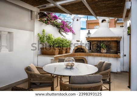 An idyllic open-air dining area unfolds with a tastefully arranged table and chairs, accompanied by a pristine white stone oven and BBQ. Ideal for conveying allure of outdoor gatherings, restaurant