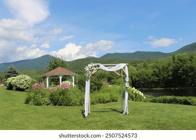 Idyllic outdoor wedding venue with floral wedding arch, picturesque gazebo, and overwatched with perfect blue skies and white clouds - Powered by Shutterstock