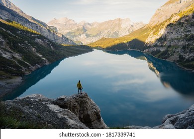 Idyllic panorama view of the lake Oeschinensee travel destination. Man tourist alone, looking at landscape of Swiss Alps. Discover the beauty of earth.