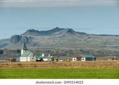 Idyllic rural landscape with church, farmhouses, and mountains under clear sky - Powered by Shutterstock