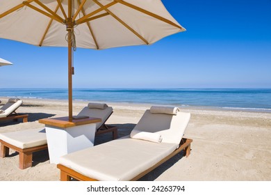 Idyllic scene of deck chairs under an umbrella on a clean beach in the hot afternoon sun.