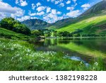 Idyllic scenery of English Lake District in springtime.Trees and grass growing on lakeshore, green hill reflecting in lake water.Sunlight kissing mountain slope in background.Majestic landscape scene.