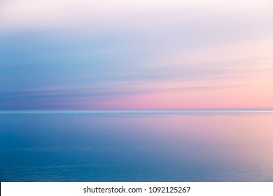 Idyllic seascape with pink evening color. The calm sea reflects the clear sky like a mirror. Blue pink sea background