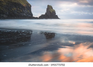 Idyllic seascape and sea stack with wet sand reflection during sunrise or sunset at Talisker Bay Beach on the Isle of Skye, Scotland