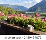 Idyllic view from balcony with geranium flowers and coffee cup in the village of Wiesing towards green valley with Alps and Lake Achensee in Tyrol, Austria. Summer sunny day