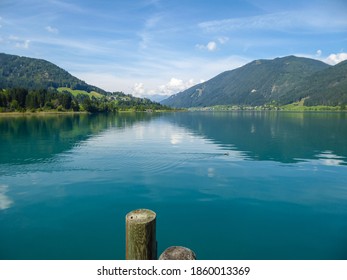 An Idyllic View On The Weissensee Lake In Austria. The Lake Is Surrounded By High Alps. The Calm Water Reflects The Mountains On It's Surface. Few Clouds Above The Peaks. Calmness And Peace