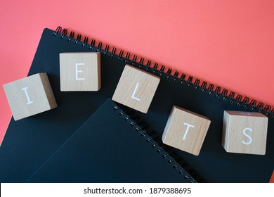 IELTS; Nine Wooden Blocks With IELTS EXAM Text Of Concept And Black Notebooks.